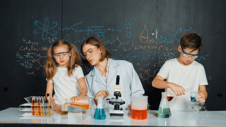 Caucasian boy mixing chemical liquid while teacher giving advice. Professional instructor wearing lab suit looking for diverse student at table with beaker filled with colored solution. Erudition.の写真素材