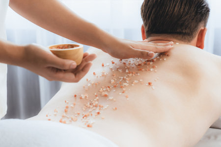 Blissful man customer having exfoliation treatment in luxury spa salon with warmth candle light ambient. Salt scrub beauty treatment in health spa body scrub. Quiescentの写真素材