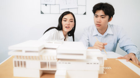 Closeup of skilled architecture engineer team measure and decide house model while working together and discussing about house structure at meeting room with blueprint placed behind. Immaculate.の写真素材
