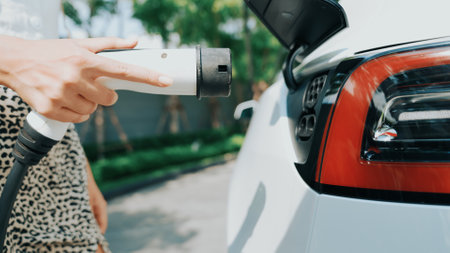 Young woman travel with EV electric car charging in green sustainable city outdoor garden in summer. Urban sustainability lifestyle by green clean rechargeable energy of electric BEV vehicle innardsの写真素材