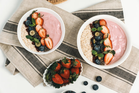 Presented by fruits putting yogurt toppings with strawberry, berry, oats, raisins and chia seed decorated by peppermint in white blow. Pink background. Set of healthy dairy product choice. Pecuniary.の写真素材