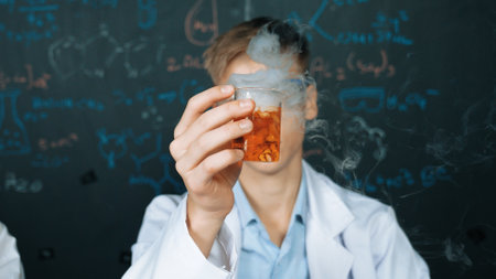 Closeup of boy inspect chemical solution while holding beaker at blackboard with chemical theory....
