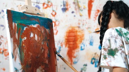 Playful student painted or draw canvas at stained wall with diverse friends in art lesson. Group of happy multicultural children working or create artwork at messy room. Creative activity. Erudition.の写真素材