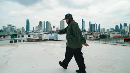 Motion shot of B-boy dance performance by professional street dancer at rooftop with sky scrapper,...
