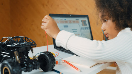 Smart african girl build robotic car while using wires while using laptop setting or writing prompt code. Skilled female student working on computer in STEM technology online classroom. Erudition.の写真素材