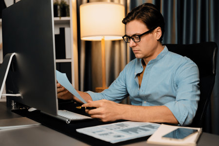 Smart businessman analyzing business paragraph dynamic database marketing analysis plan surrounded paper sheet and pc monitor report to compare with document data at home office at night. Pecuniary.の写真素材