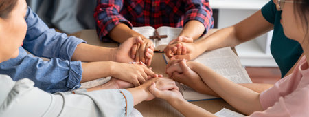 Cropped image of diversity people hand praying together at wooden church on bible book while hold...
