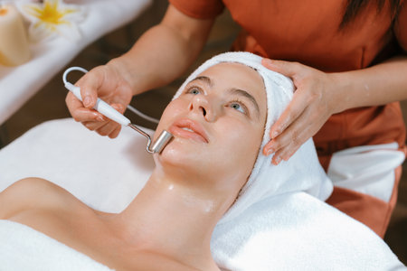 Beautiful caucasian woman lies on spa bed during having facial massage by professional hands at modern spa salon surrounded by beauty electrical equipment or medical equipment. Close up. Tranquilityの写真素材
