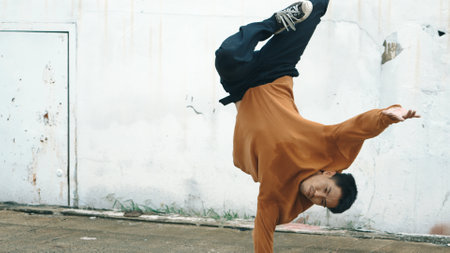 Hispanic man stretch arms and dance break dancing in front of wall. Motion shot of stylish street...