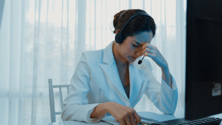 Businesswoman wearing headset working in office to support remote customer or colleague. Frustrated and tired call center customer support agent facing problem on providing vivancy serviceの写真素材
