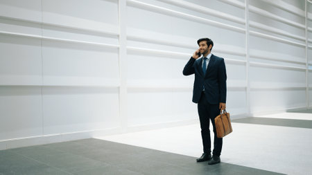 Skilled manager using phone call to contact colleague about project. Handsome male leader calling his business team to report and discuss about sales while standing at white background. Exultant.の写真素材