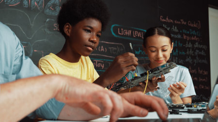 Young student fixing controller while teacher programing engineering code at STEM class. Closeup of...