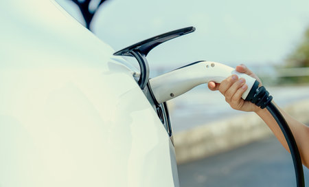 Kids hand insert EV charger plug into electric vehicle, recharge EV car battery from outdoor...