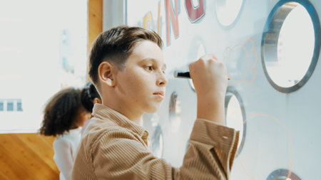 Closeup of caucasian creative student draw beautiful picture at glass board in art lesson. Smart boy...