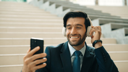 Happy smart business man taking selfie while smiling at smart phone. Closeup image of professional executive manager sitting at stairs while wearing suit and headphone. Creative business. Exultant.の写真素材