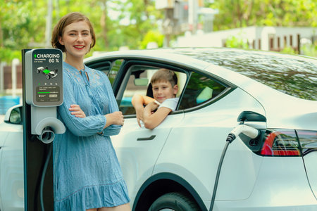 Environmental awareness family with eco-friendly electric car recharging battery from home EV charging station with little boy inside the car. Rechargeable and EV car technology. Perpetualの写真素材