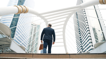 Smart caucasian businessman walking up stairs surrounded by urban view. Back view of ambitious project manager finding challenging job or investment opportunity at city with modern building. Urbane.の写真素材