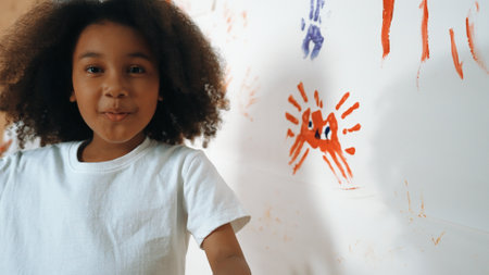 Smiling smart african girl looking at camera while standing at stained wall in art lesson. Young...