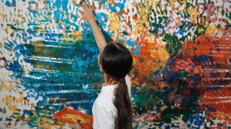 Young happy girl holding the color tray and paint colorful stained wall to express idea and enhance imagination with hand print. Caucasian girl stamp hand to decorate room in art lesson. Edification.の写真素材