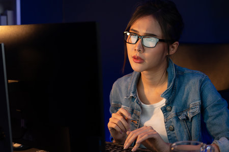 Portrait young beautiful Asian creative with glasses of serious face looking on pc to search project creator social media online, planning strategy creator at neon modern office at night. Stratagem.の写真素材