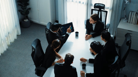 Top view of manager raised hand and present financial graph while holding tablet. Diverse group...
