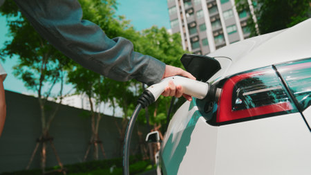 Young man recharge EV electric car battery at residential area EV charging station in urban city...