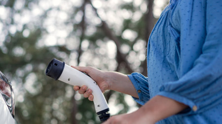 Closeup woman recharge EV electric cars battery at parking lot in natural green park. Clean energy technology for rechargeable vehicle for sustainable and eco friendly travel. Perpetualの写真素材