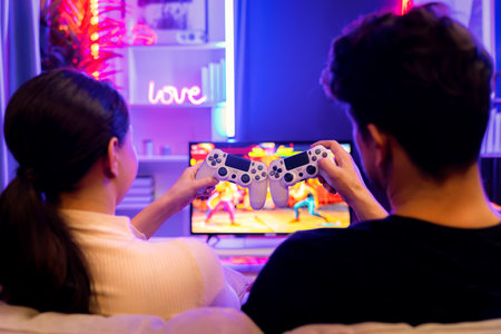 Couple or friend buddy joyful player video game on TV using joysticks to bring together at back side view, winner with blurry screen in studio room in neon cyber light at comfy living home. Postulate.の写真素材