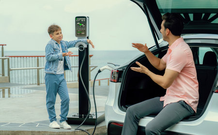 Family road trip vacation traveling by the sea with electric car, father and son recharge EV car with green and clean energy. Natural travel and eco-friendly car for sustainable environment. Perpetualの写真素材