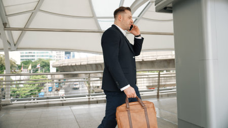 Smart caucasian businessman calling his colleague to plan financial strategy while walking to workplace. Side view of manager using mobile phone to communicate with marketing team. Lifestyle. Urbane.の写真素材