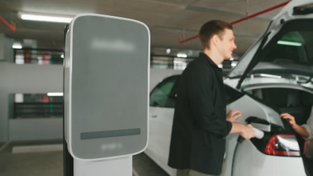 Young couple travel with EV electric car to shopping center parking lot charging in downtown city...