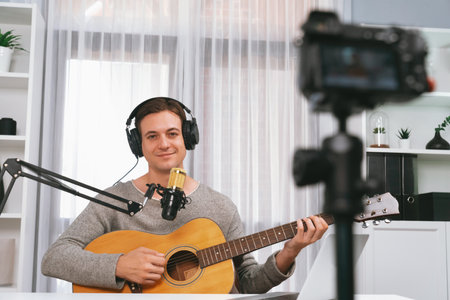 Host channel in smart singer recording by camera, playing guitar along singing, broadcasting on social media channel, wearing headphones to record video streamer at white modern studio. Pecuniary.の写真素材