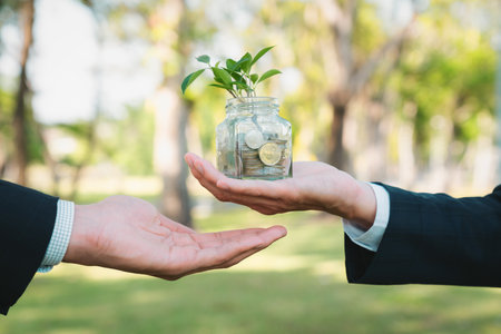 Concept of sustainable money growth investment with glass jar filled with money savings coins with businesspeople as eco-friendly financial investment nurtured with nature and healthy retirement. Gyreの写真素材