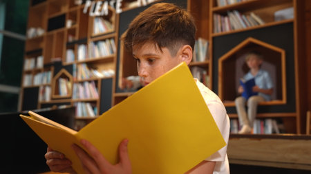 Caucasian boy reading a book while group of smart students sitting at library. Attractive child studying, learning from novel or textbook while children talking, chitchat about education. Erudition.の写真素材