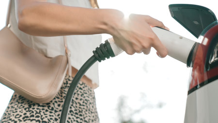 Sunlight backlit brighten young woman travel with EV electric car charging in green sustainable city outdoor garden in summer. Green urban sustainability lifestyle by electric vehicle innardsの写真素材