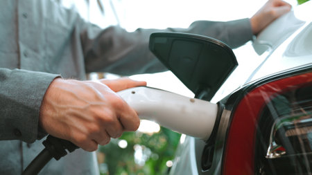 Young man recharge EV electric car in green sustainable city outdoor summer garden as lifestyle of young people in urban sustainability green clean rechargeable energy of electric vehicle innardsの写真素材