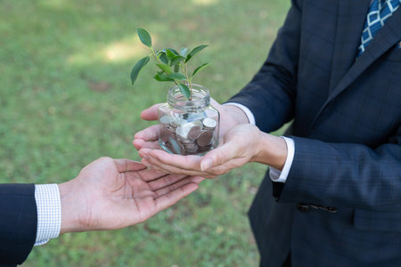 Concept of sustainable money growth investment with glass jar filled with money savings coins with businesspeople as eco-friendly financial investment nurtured with nature and healthy retirement. Gyreの写真素材