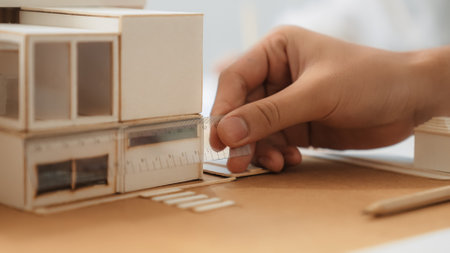 Closeup image of skilled professional engineer hand using ruler measures house model on table with...