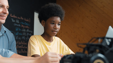 African boy using laptop to program code or prompt with car model placed while teacher and caucasian friend study about robotic construction. Student study about car model structure. Edification.の写真素材