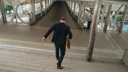 Businessman walking down stair and hurry to walking back to home. Back view of business people wearing suit and celebrate for getting promotion or increasing sales while holding his suitcase. Urbane.の写真素材