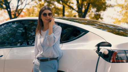 Woman using smartphone online banking application to pay for electric car battery charging from EV charging station during vacation holiday road trip at national park or summer forest. Exaltの写真素材