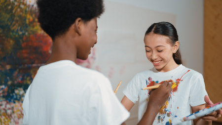 Smiling diverse children using paint brush painted color on each other white shirt shirt at colorful...