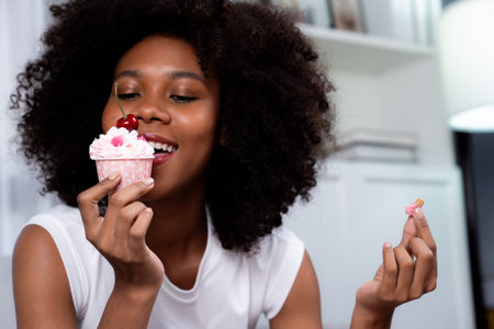 Portrait of beautiful young African blogger tasting piece of cherry cake in concept special cuisine. Presenting cute cupcake decorate fruit for content creating on social media. Tastemaker.の写真素材