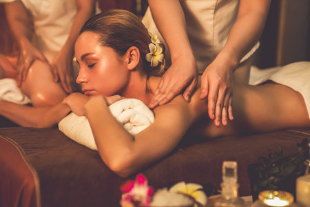 Caucasian couple customer enjoying relaxing anti-stress spa massage and pampering with beauty skin recreation leisure in warm candle lighting ambient salon spa at luxury resort or hotel. Quiescentの写真素材