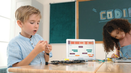 Girl standing while fixing electronic board by using screwdriver. American student and happy caucasian boy working together to inspect electric system. Curious children working on board. Pedagogy.の写真素材