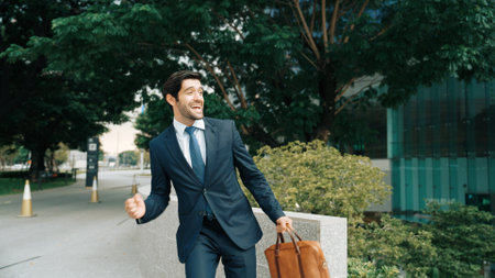 Smart business man walking along the road while holding bag at park. Professional project manager smiling while traveling in lively mood. Happy investor getting a promotion. Business dance Exultant.の写真素材