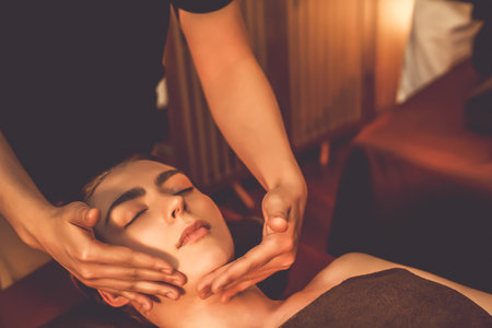 Caucasian woman enjoying relaxing anti-stress head massage and pampering facial beauty skin recreation leisure in warm candle lighting ambient salon spa in luxury resort or hotel. Quiescentの写真素材