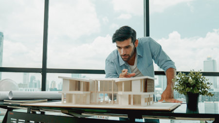 Smart caucasian engineer or project manager measure check, inspect, look at house model while standing near panorama window with city, skyscraper view. Manager design house construction. Traceryの写真素材