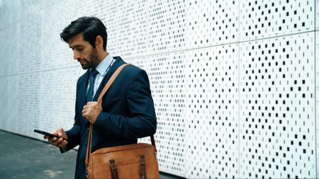 Smart manager looking at mobile phone and walking at street while wearing suit. Skilled investor looking mobile phone to checking sales or working while holding coffee cup. White background. Exultant.の写真素材