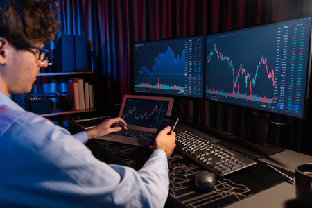 Working young business trader focusing on smartphone comparing with laptop in market stock graph in...